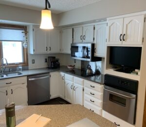 Worn, all-white kitchen in Fargo, ND featuring dated beadboard cabinet doors and aged finishes—captured prior to the Kitchen Refresh transformation.